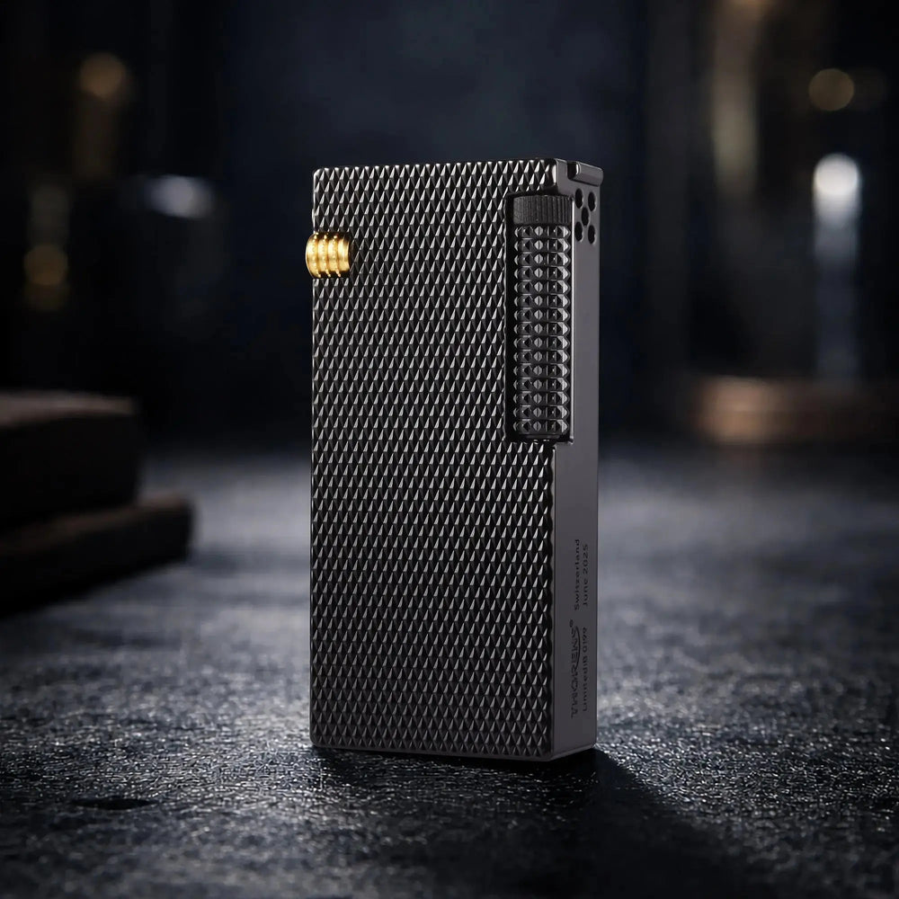 A professional still life shot of the Thorens Slim Cube lighter in Black Mesh finish, standing on a textured dark surface. The image highlights the intricate diamond-patterned mesh texture, gold-toned mechanical accents, and the limited edition "Thorens Switzerland" engraving on the side, reflecting a premium EDC aesthetic.
