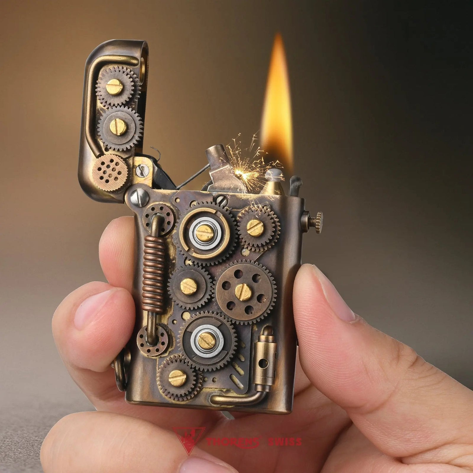 A hand holding an ignited Thorens Steampunk-Abyss Coil lighter, showing the sparks and flame against its intricate brass gear and coil structure.
