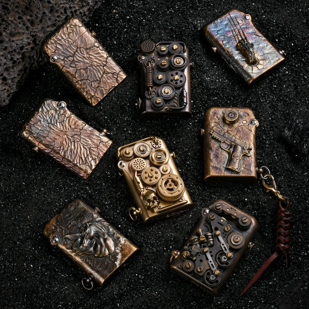 A group of Thorens lighters, including the Steampunk-Twin Torque with brass gears and various hand-carved textured designs, resting on black sand.