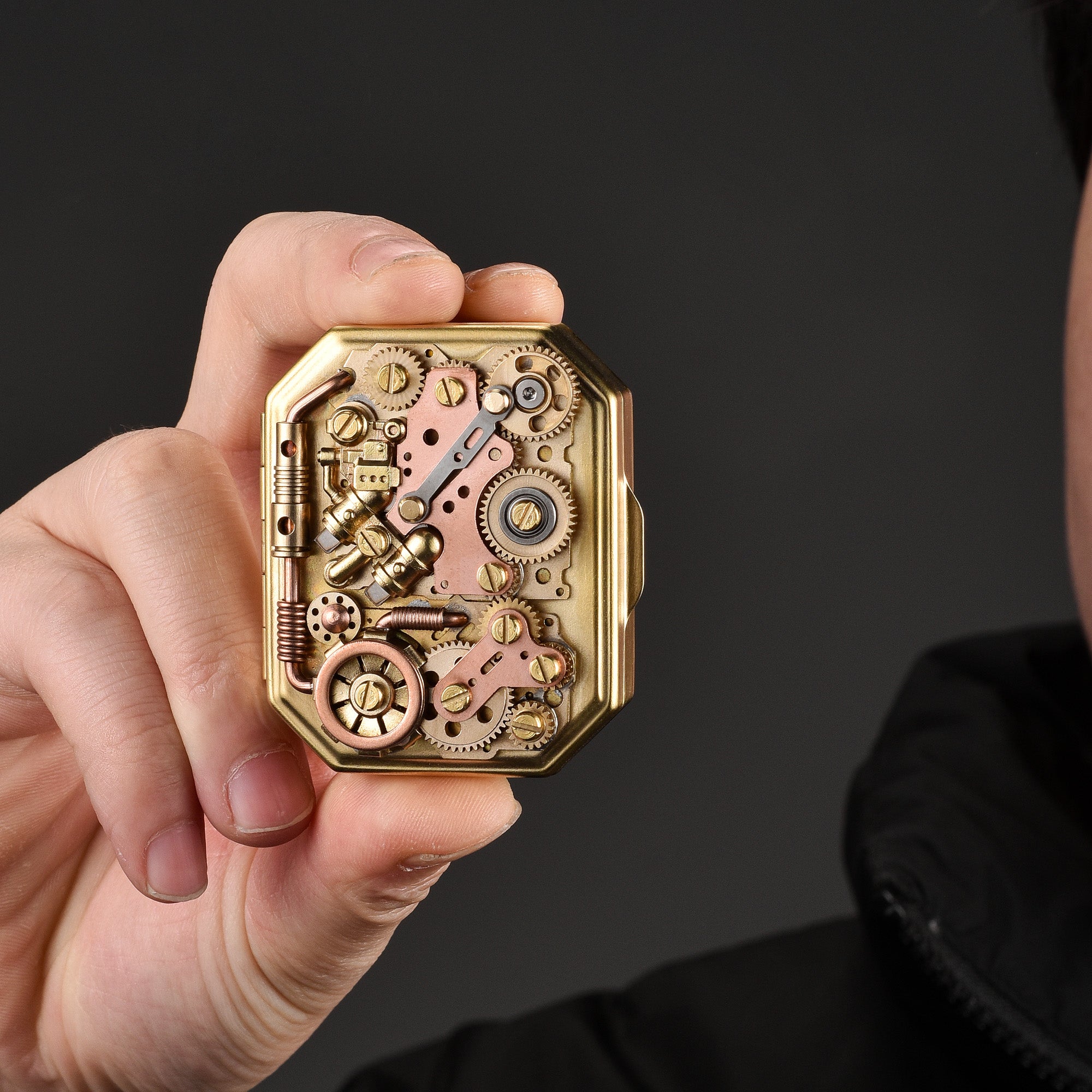 Thorens Steampunk Matchbox Twin Torque lighter held in hand, showing exposed brass gears, copper plates, and intricate mechanical components.
