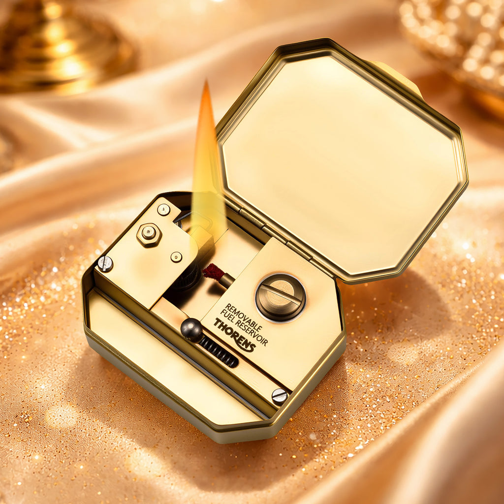 Thorens Steampunk Matchbox Twin Torque lighter open and lit, showing flame, brass inner structure, and removable fuel reservoir on a vintage textured surface.