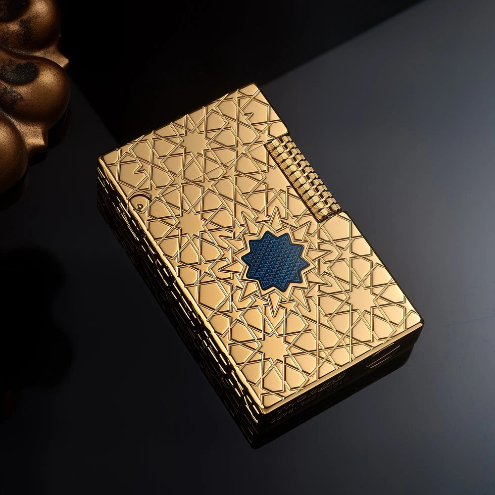 A top-down view of the Thorens Stellar Mesh Gold lighter on a dark reflective surface, showcasing the precise geometric star engraving and blue mesh inlay.