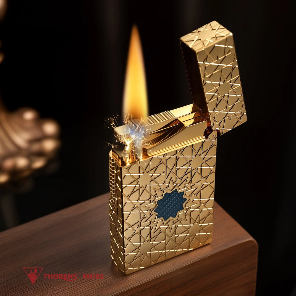 A Thorens Stellar Mesh Gold lighter with an open lid, captured during ignition to show the flint spark and flame against the gold geometric star pattern.