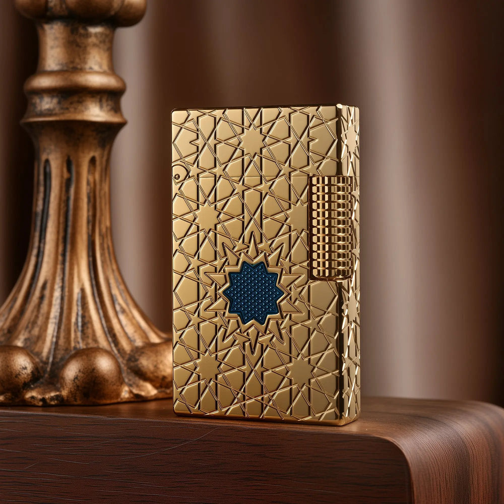 A Thorens Stellar Mesh Gold lighter featuring an intricate geometric star engraving and a central blue mesh inlay, resting on a polished wood surface next to a vintage pedestal.