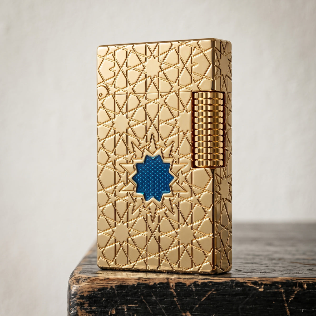 A Thorens Stellar Mesh Gold lighter featuring an intricate geometric star engraving and a central blue mesh inlay, resting on a polished wood surface next to a vintage pedestal.