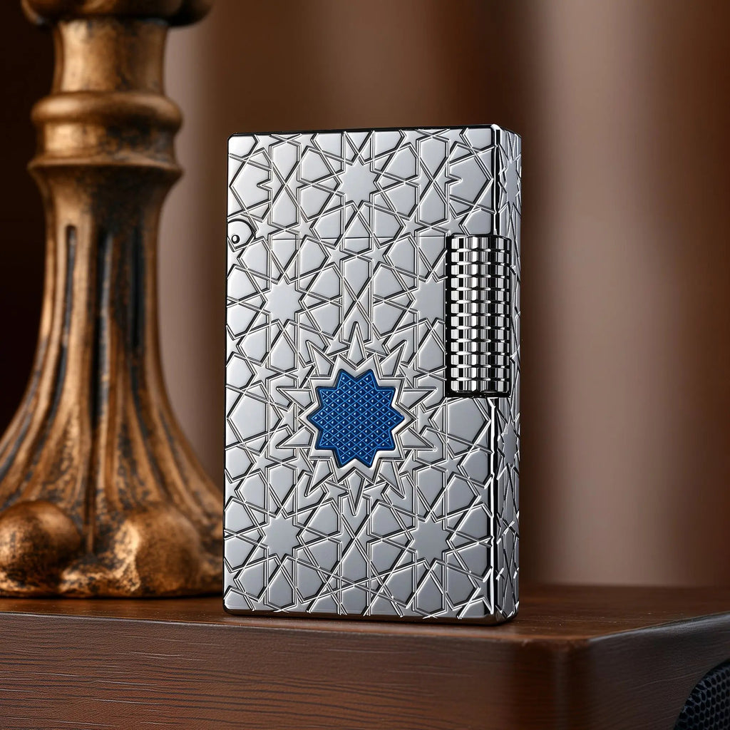 A Thorens Stellar Mesh Silver lighter featuring an intricate geometric star engraving and a central blue mesh inlay, resting on a polished wood surface next to a vintage pedestal.