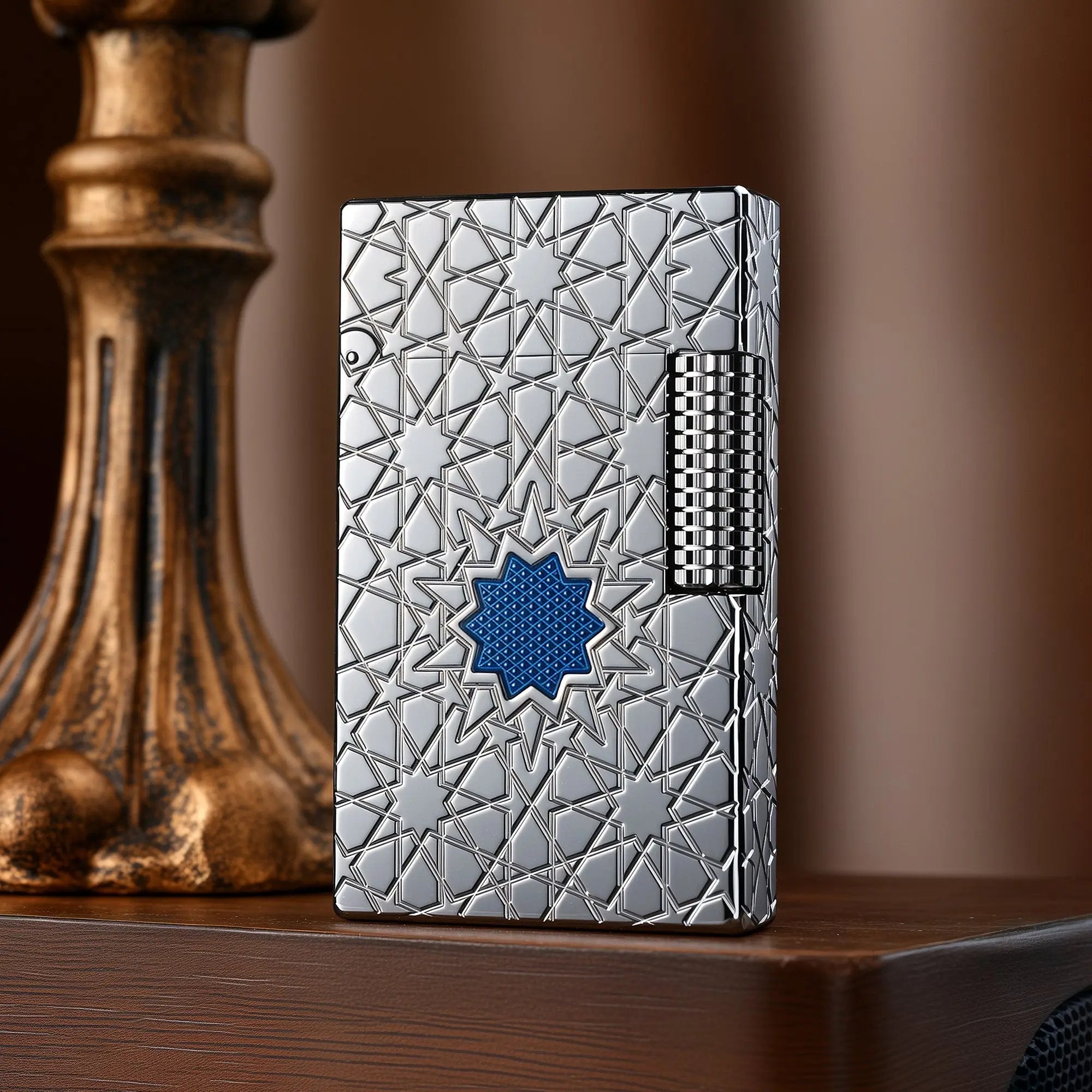 A Thorens Stellar Mesh Silver lighter featuring an intricate geometric star engraving and a central blue mesh inlay, resting on a polished wood surface next to a vintage pedestal.