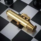 A brushed brass trench lighter in a unique submarine-inspired shape, resting on a black and white chessboard with mechanical adjustment screws and a sun logo engraving.