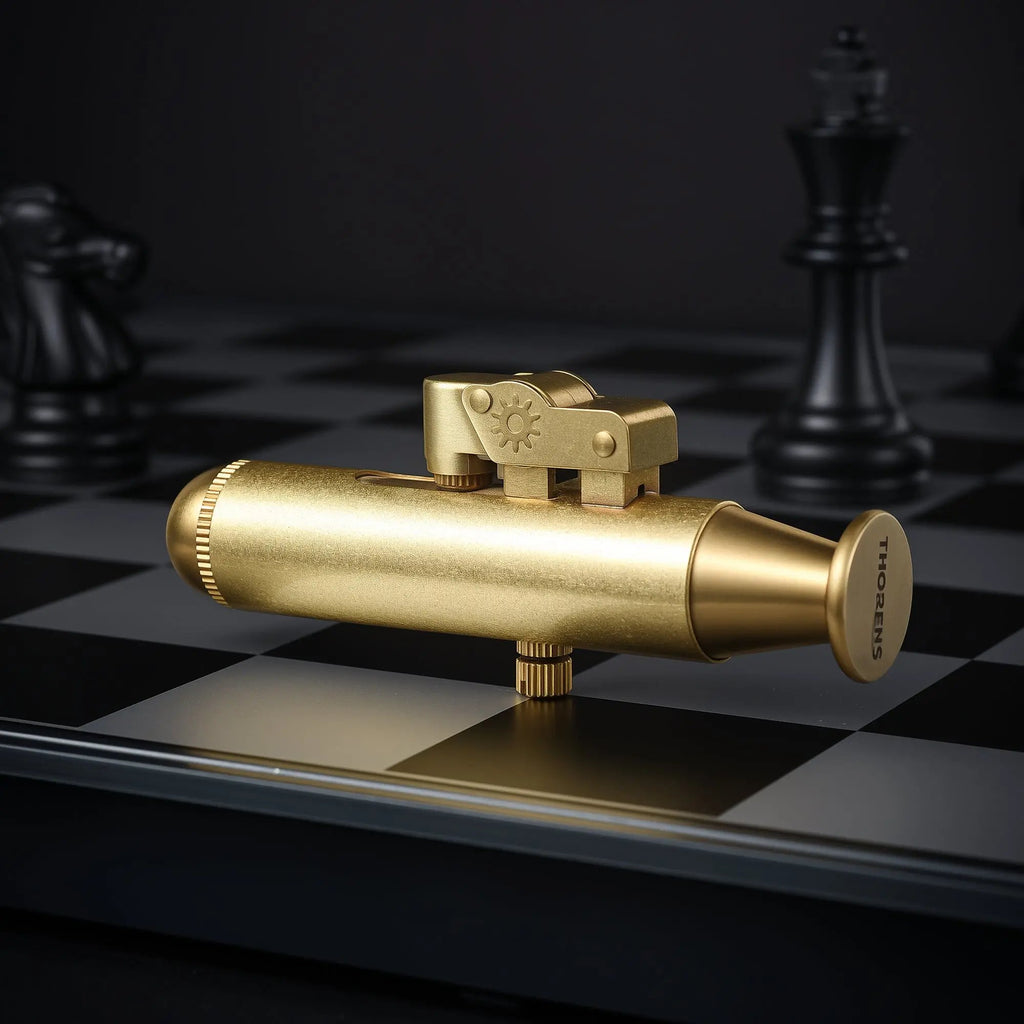 A horizontal side view of the Submarine trench lighter in brushed brass, showcasing its unique nautical silhouette and mechanical thumb-lever on a chessboard.