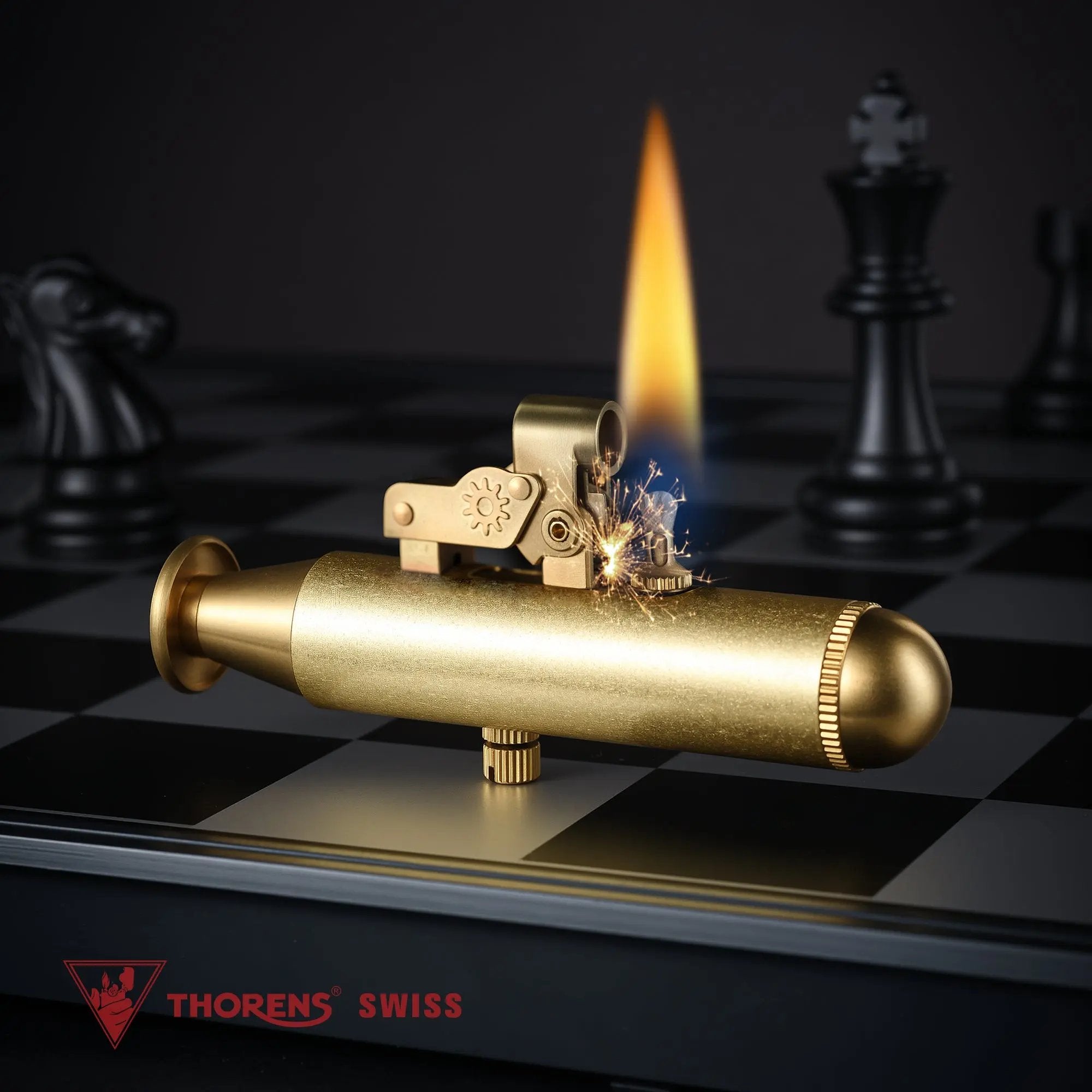 An ignited Submarine trench lighter in brass showing a tall vertical flame and bright sparks from the flint wheel, set on a dark chessboard background.