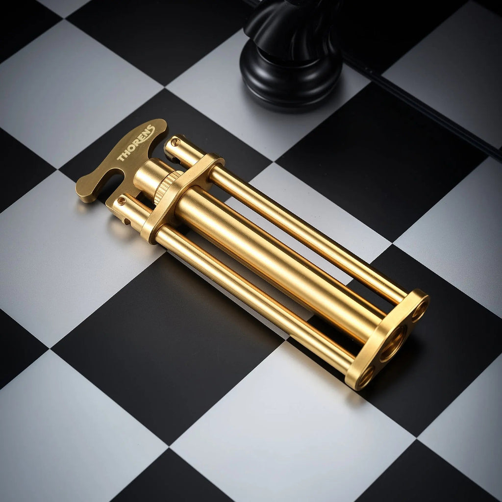 A Three-Section Stick Lighter with a brushed brass finish and engraved Thorens logo, laid diagonally across a black and white checkered surface.