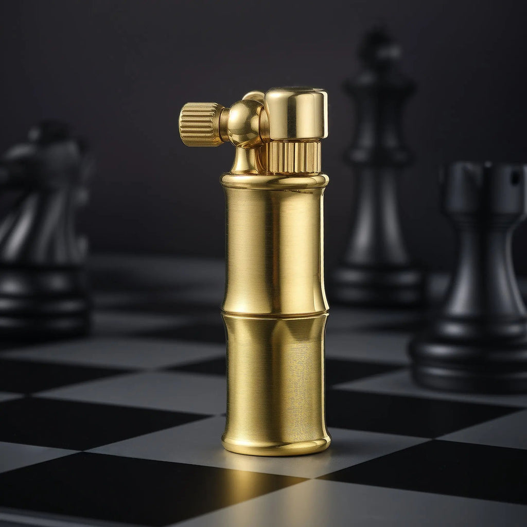 A vertical studio shot of the Mini Bamboo lighter in brushed brass, standing on a silver and black chessboard with out-of-focus black chess pieces in the background.