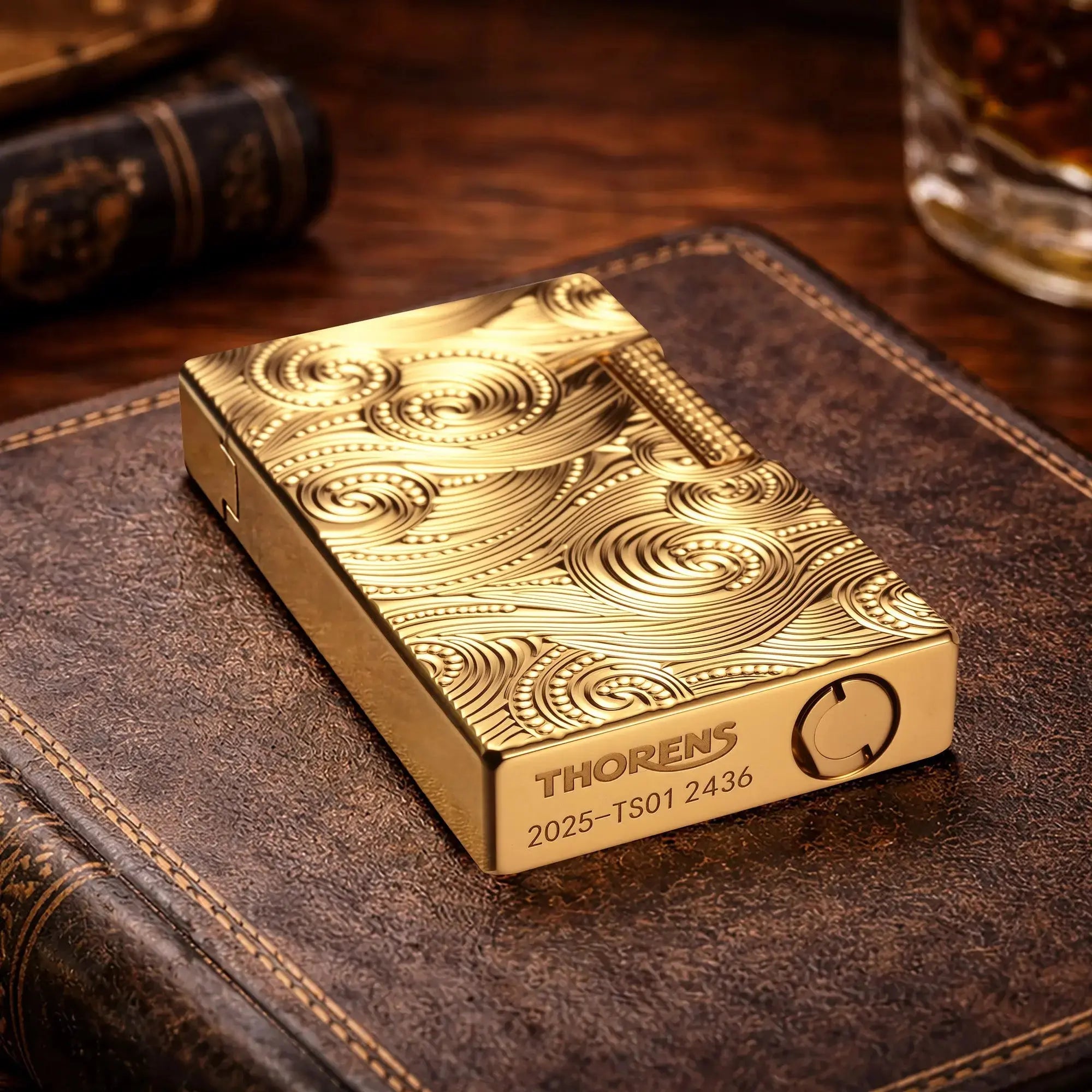 A close-up of a gold Thorens vortex-engraved lighter resting on a leather surface, highlighting the authentic brand logo and serial number engraved on the bottom.